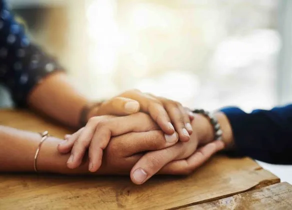Gros plan sur deux personnes se tenant la main, symbolisant l'écoute, le soutien dans le deuil.