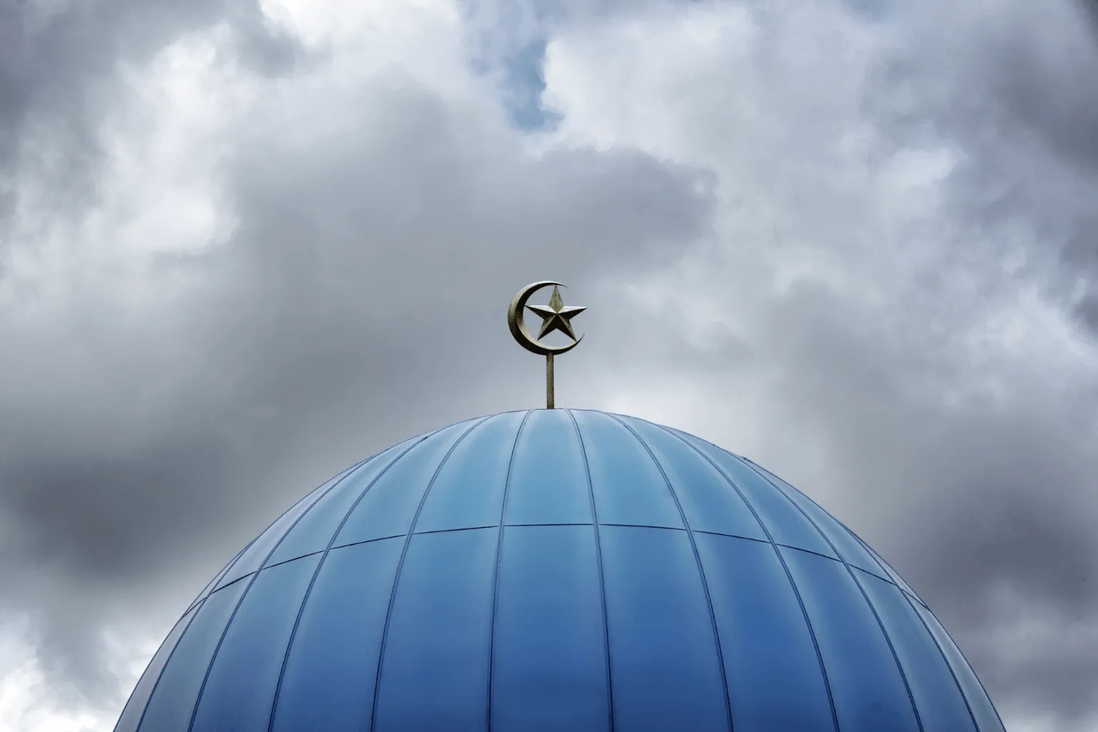 Dôme bleu d'une mosquée surmonté d'un croissant et d'une étoile sous un ciel nuageux.